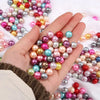 A hand holds a cluster of colorful imitation pearl beads in various shades of pink, blue, and gold for DIY jewelry making.