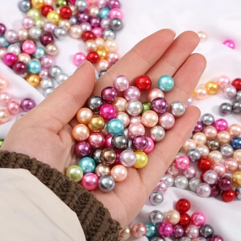 A hand holds a cluster of colorful imitation pearl beads in various shades of pink, blue, and gold for DIY jewelry making.