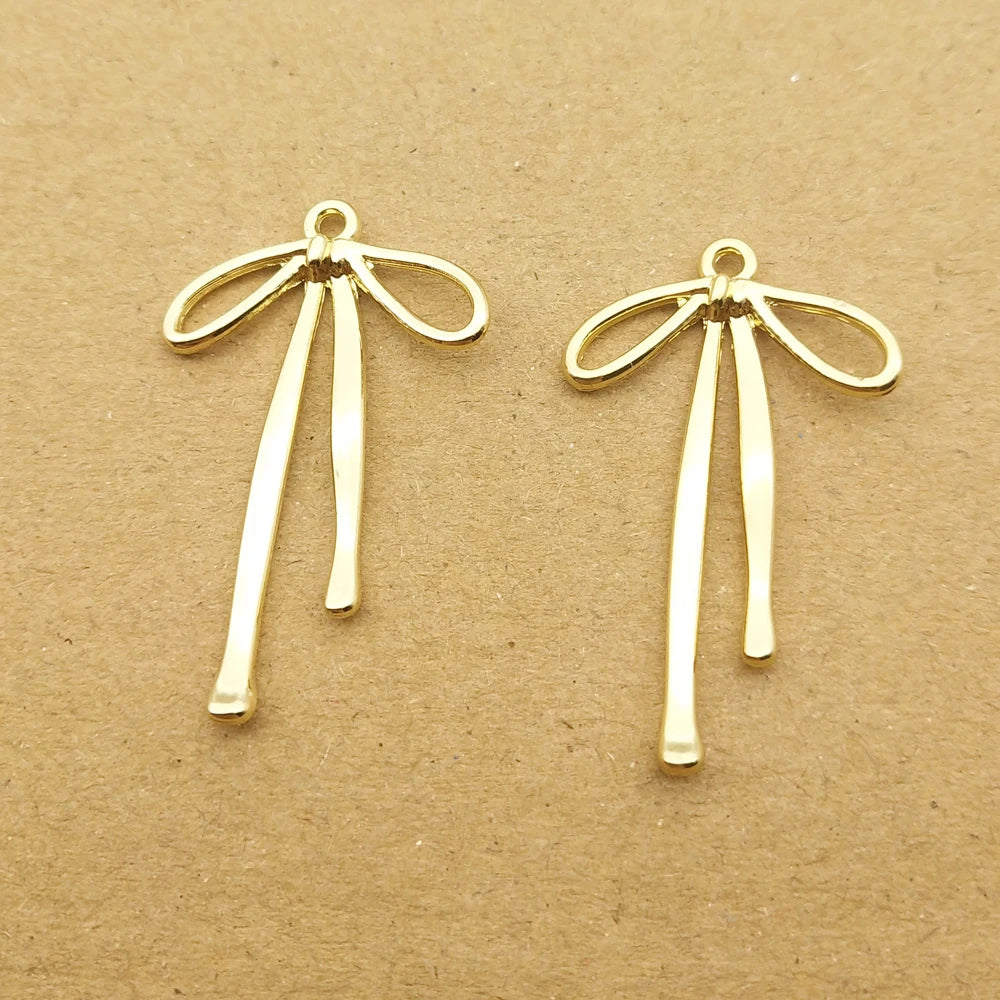 A pair of gold-colored alloy bow charms for jewelry making displayed on brown paper.