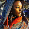A close-up portrait of an African woman wearing a patterned headscarf and orange shawl, looking to the side.