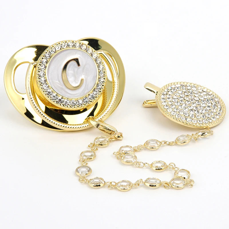 Gold and clear rhinestone pacifier featuring a personalized initial charm on a clip.