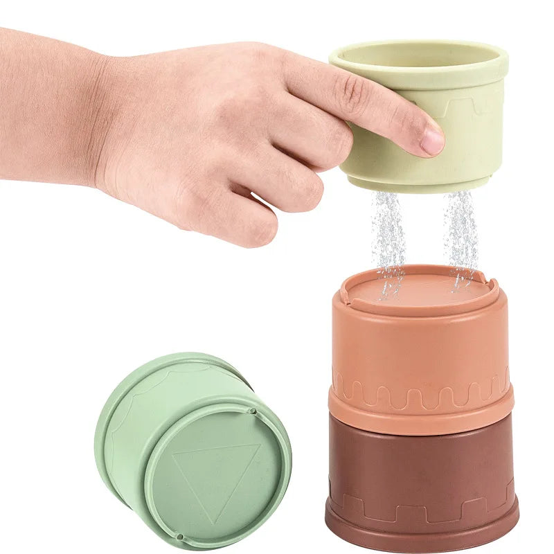 A hand is pouring water from a light green cup into a larger terracotta-colored stacking cup set for toddlers.