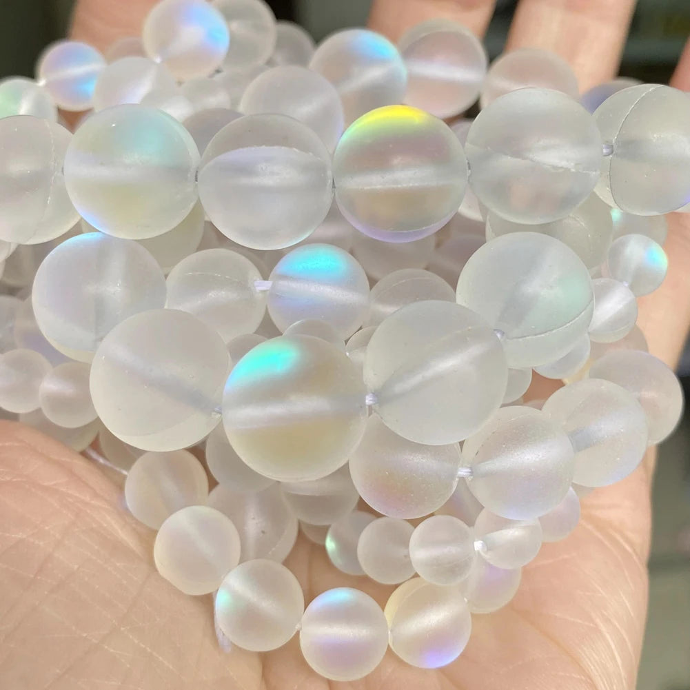 A collection of translucent, iridescent natural gemstone beads in various shades of white and pale blue are held in a hand.