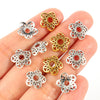 A hand holds several small, gold and silver Tibetan style hollow flower bead caps for jewelry making.