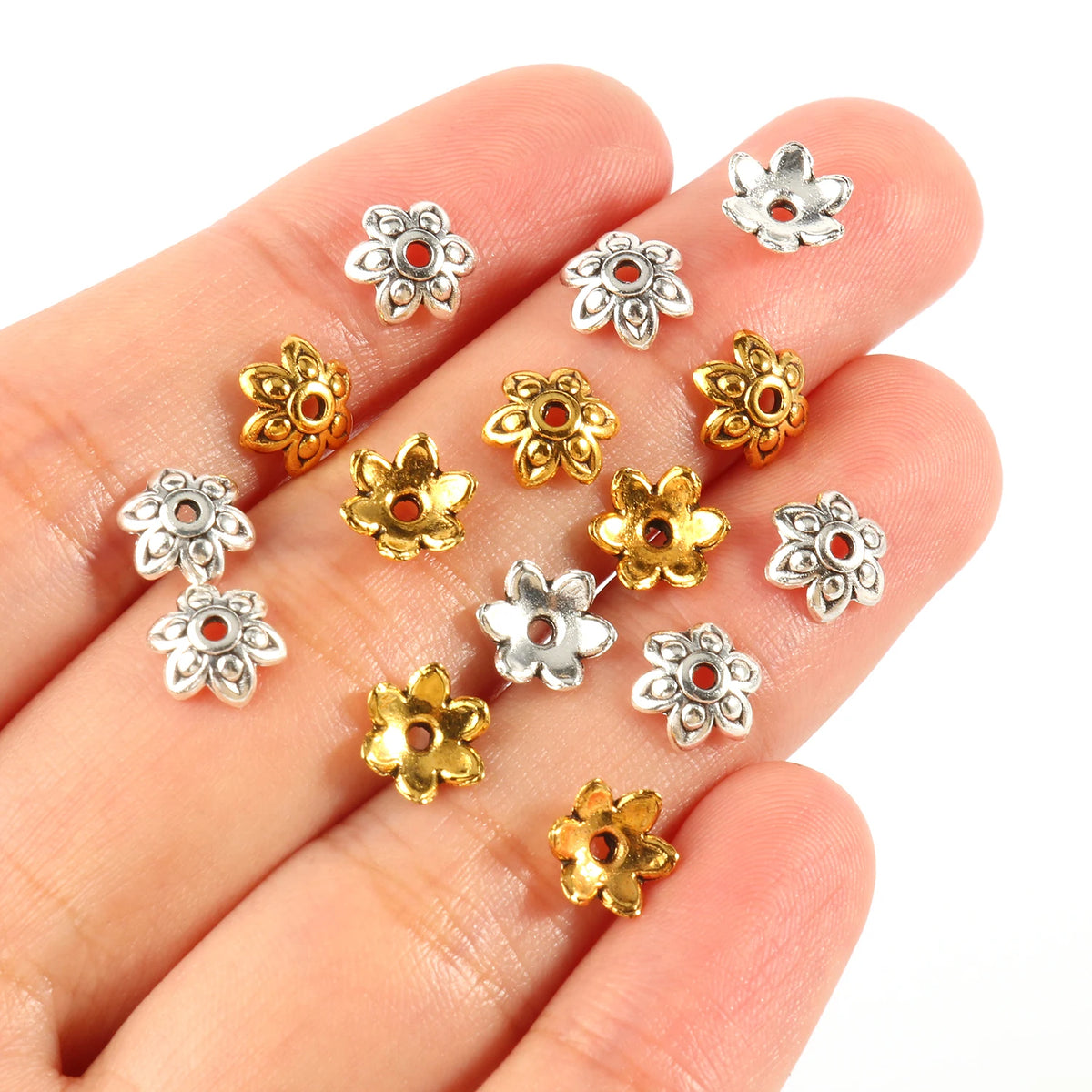 A hand holds several silver and gold Tibetan style hollow flower bead caps for jewelry making