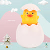 A yellow duck toy is emerging from a pink egg-shaped container, set against a light blue background.