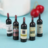 A set of five miniature resin wine bottles with dark liquid and labels displayed on a light blue surface.