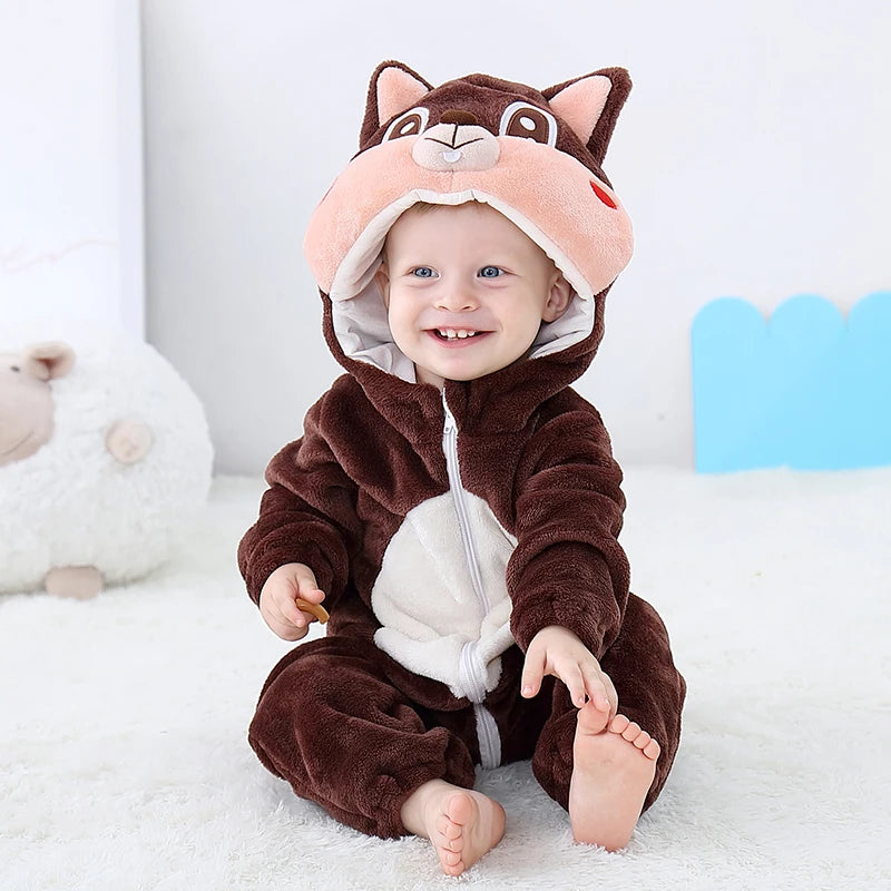 A baby wearing a brown hooded romper with pink ears and a white chest detail, sitting on a white surface.