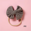 A gray knitted bow headband with a light beige elastic band is displayed on a pink background.