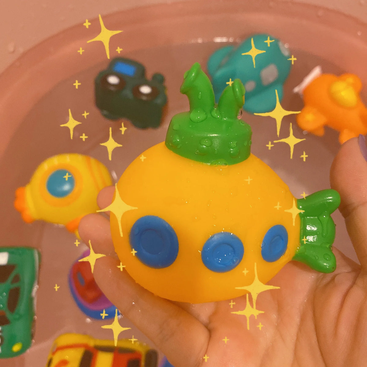 A hand holds a bright yellow rubber bath toy shaped like an animal, surrounded by other colorful toys.