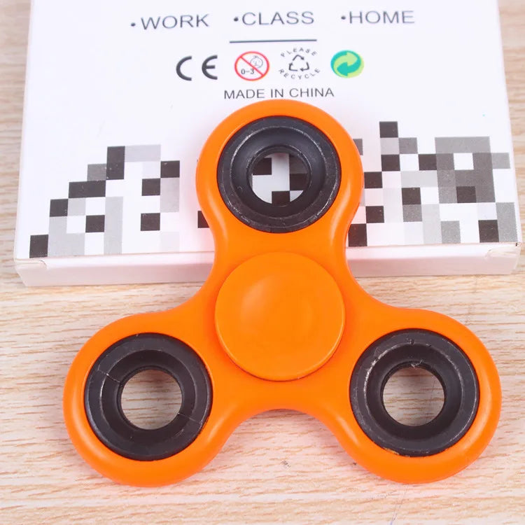 An orange ABS tri-spinner fidget toy with black rings, packaged on a white box.