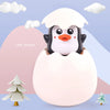 A cute little penguin toy emerging from a white egg, set against a light purple background.