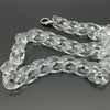 Clear acrylic bag chain strap with clips laid out on a dark surface.