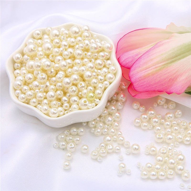 A pile of small, off-white pearl beads is displayed in a white dish next to a pink flower.
