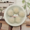 A white bowl filled with fluffy, cream-colored mink fur pom poms for crafts and accessories.