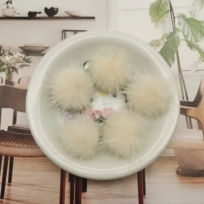 A white bowl filled with fluffy, cream-colored mink fur pom poms for crafts and accessories.