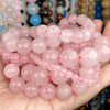 A hand holds a large collection of pink and clear gemstone beads for jewelry making.