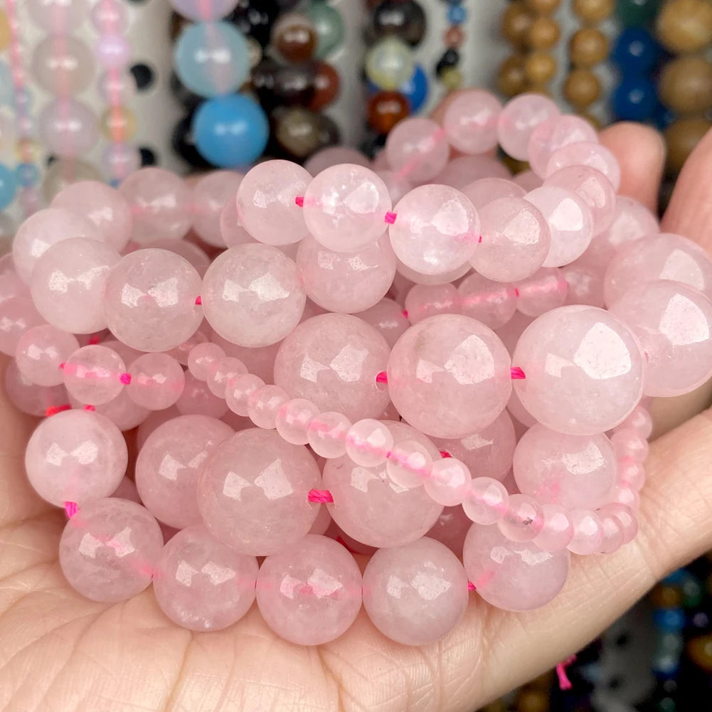 A hand holds a large collection of pink and clear gemstone beads for jewelry making.