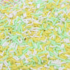 A close-up view of yellow and light green soft polymer clay candy sprinkles scattered on a surface.