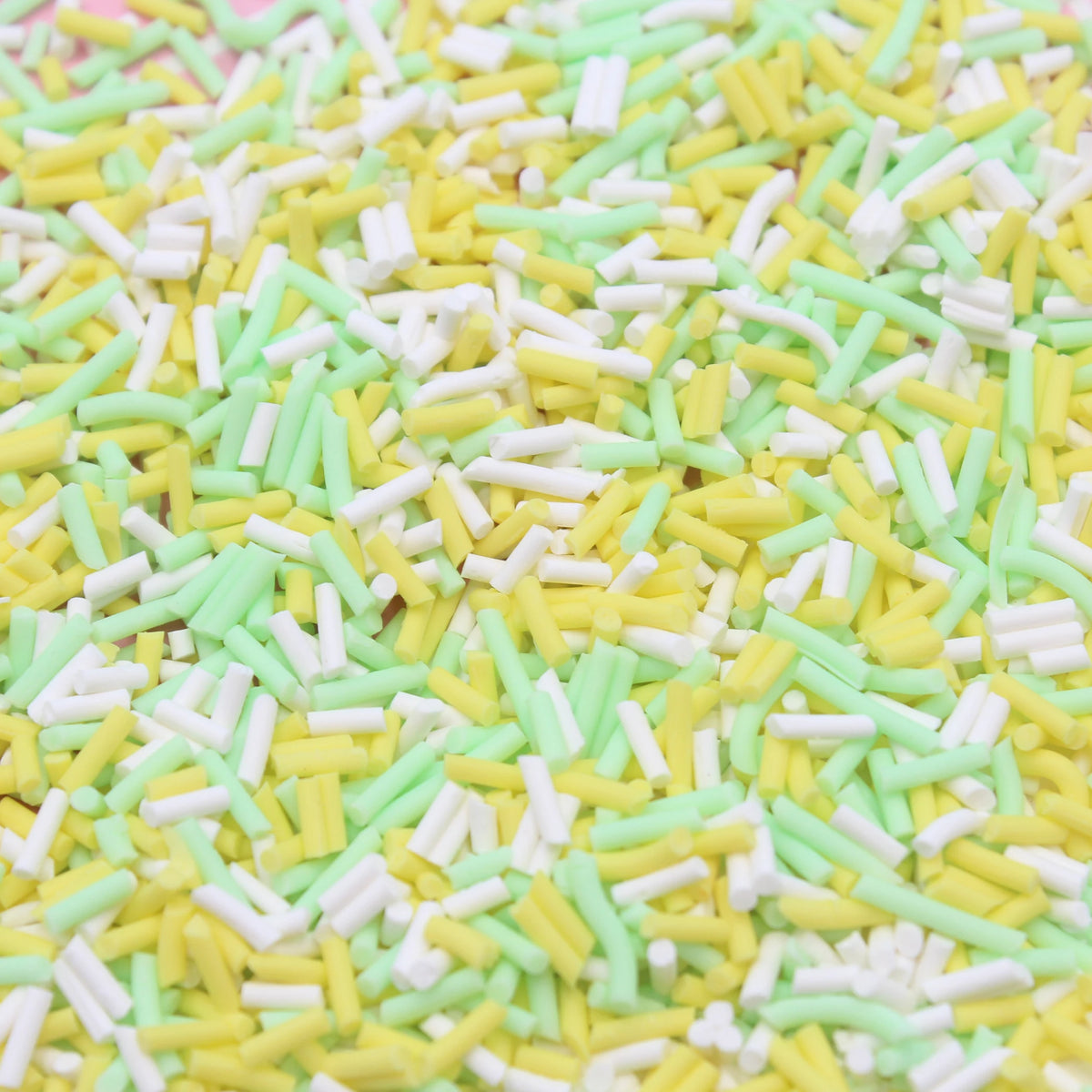 A close-up view of yellow and light green soft polymer clay candy sprinkles scattered on a surface.