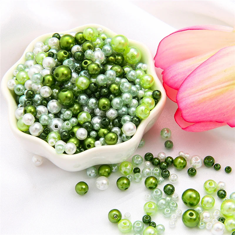 A pile of assorted green and white pearl beads for jewelry making next to a pink lotus flower.