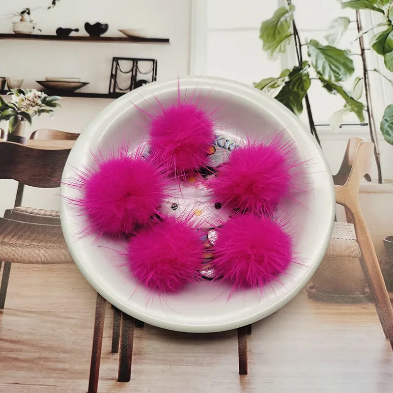 A white bowl filled with bright pink fluffy mink fur pom poms for crafting.