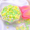 A pile of assorted light green and yellow pearl beads for jewelry making displayed on white fabric.