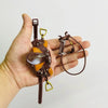 A brown leather horse saddle and riding prop accessory is held in a hand against a white background.