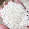 A hand holds a pile of small, white natural beeswax pellets for DIY candle making and skincare.