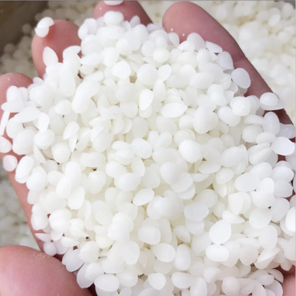 A hand holds a pile of small, white natural beeswax pellets for DIY candle making and skincare.