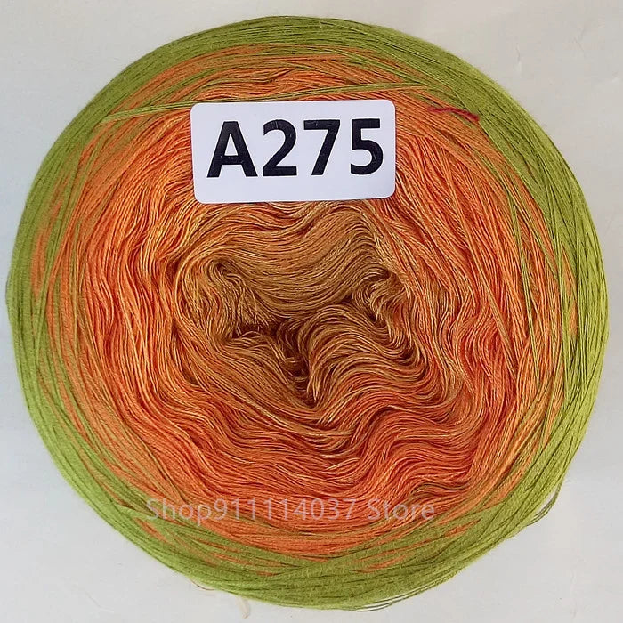 A ball of rainbow gradient mercerized cotton cake yarn showing various shades of orange, green, and yellow fibers.