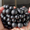 A hand holds a cluster of small, dark, spherical gemstone beads for jewelry making.