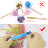 A hand holds a blue silicone stir stick with colorful pigment on a pink floral background.