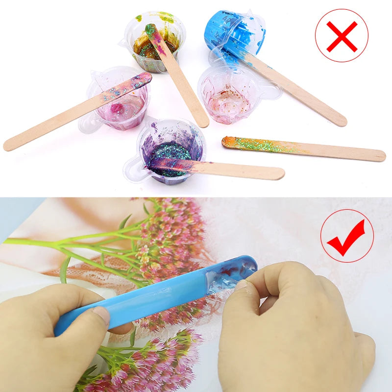 A hand holds a blue silicone stir stick with colorful pigment on a pink floral background.