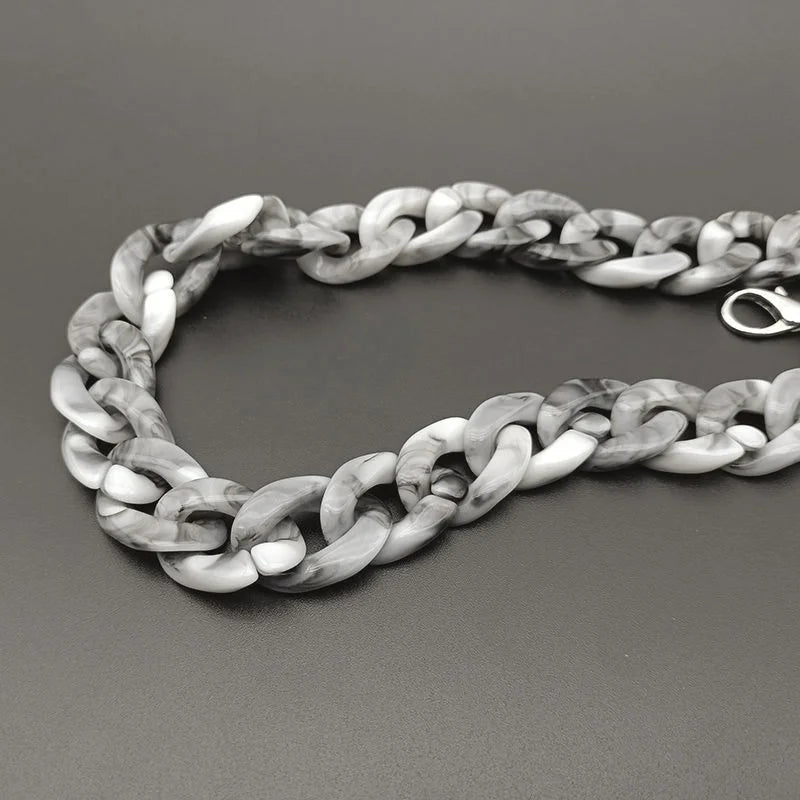 A silver and white marbled acrylic bag chain strap with clips laid out on a dark surface.