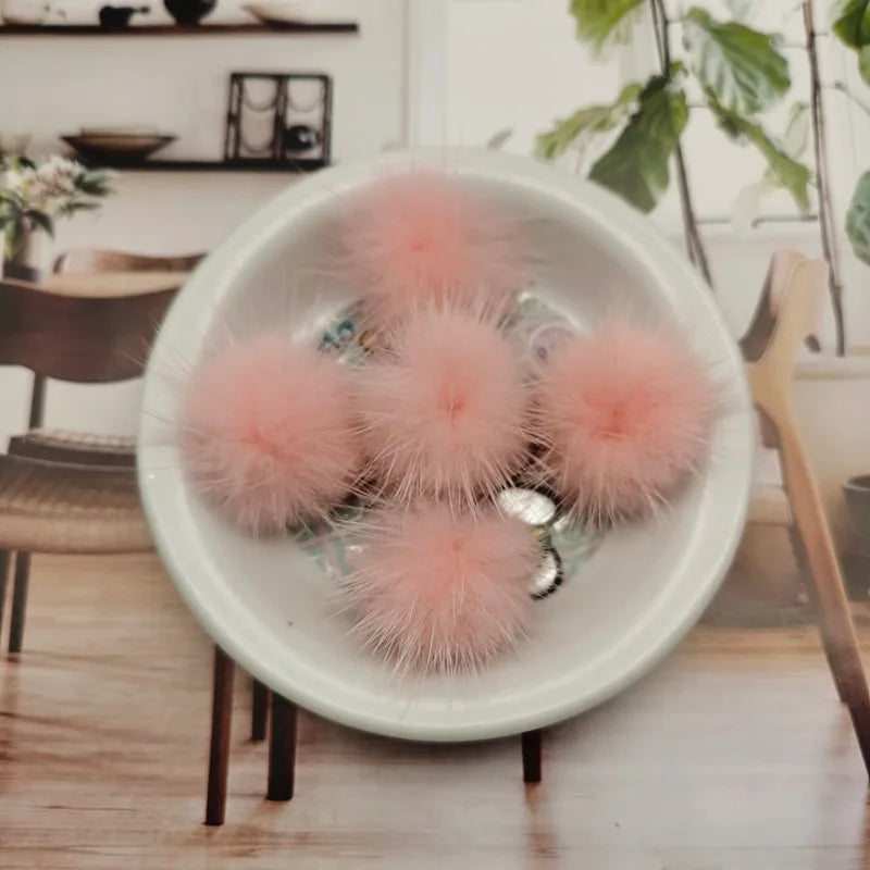 A white bowl filled with pink fluffy mink fur pom poms for crafts and accessories
