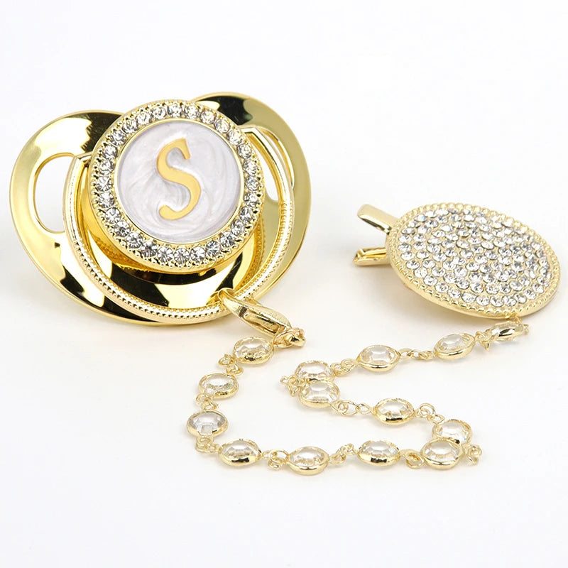 Gold and clear rhinestone pacifier featuring a silver initial on a silicone disc with a clip.