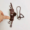 A brown leather dollhouse horse saddle and riding prop accessory being held by a hand.