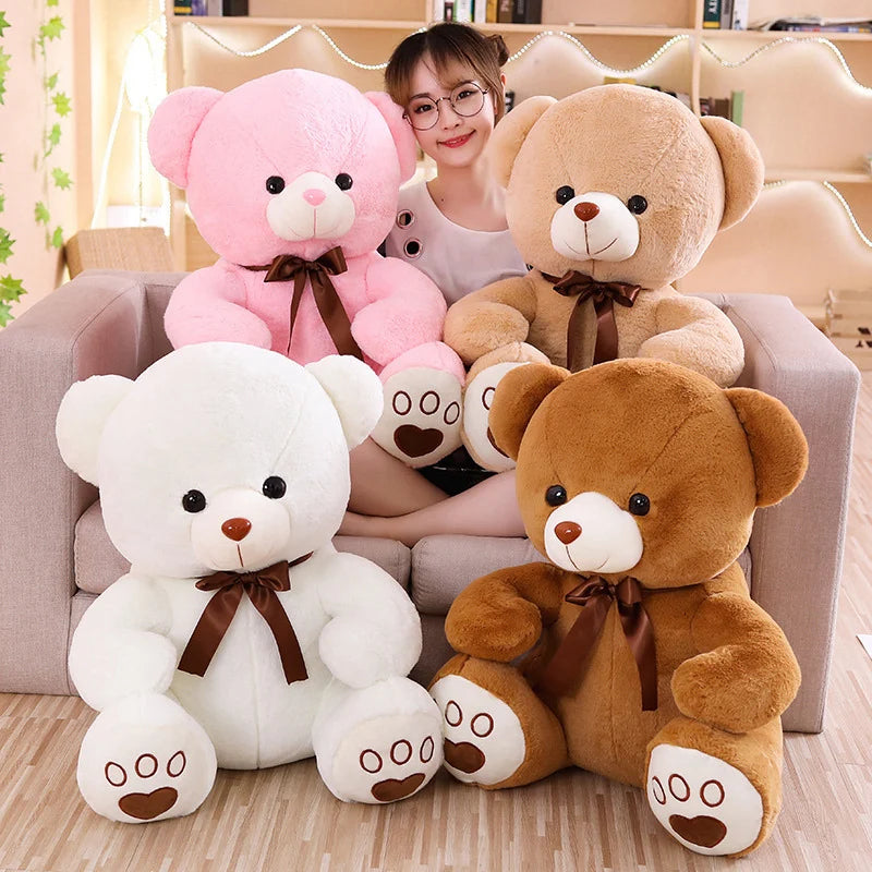 A collection of four soft plush cartoon teddy bears in pink, tan, white, and light brown sitting on a sofa.