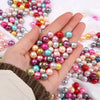 A hand holds a cluster of colorful imitation pearl beads for DIY jewelry making.