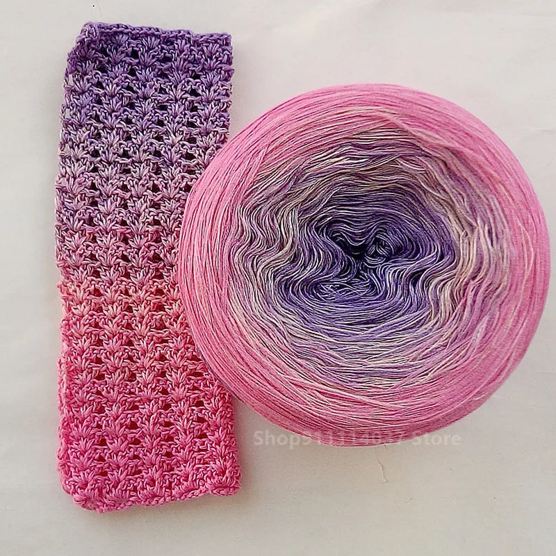 Spool of rainbow gradient mercerized cotton cake yarn showing pink and purple colors.