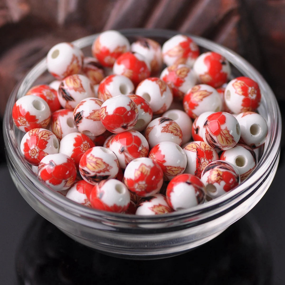 A bowl filled with small, round ceramic beads featuring a red and white floral pattern for jewelry making