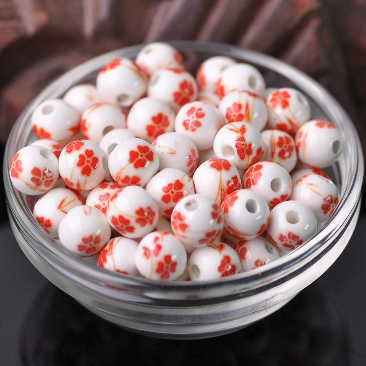 A clear glass bowl filled with small white ceramic beads decorated with red floral patterns.