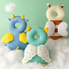 Three soft baby head protector pillows in blue, green, and white with adjustable straps resting on a fluffy white surface.