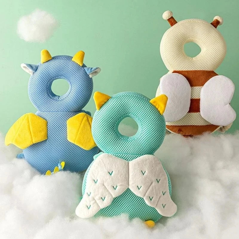 Three soft baby head protector pillows in blue, green, and white with adjustable straps resting on a fluffy white surface.