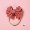 A pink knitted bow headband with a light yellow elastic band on a pink background.