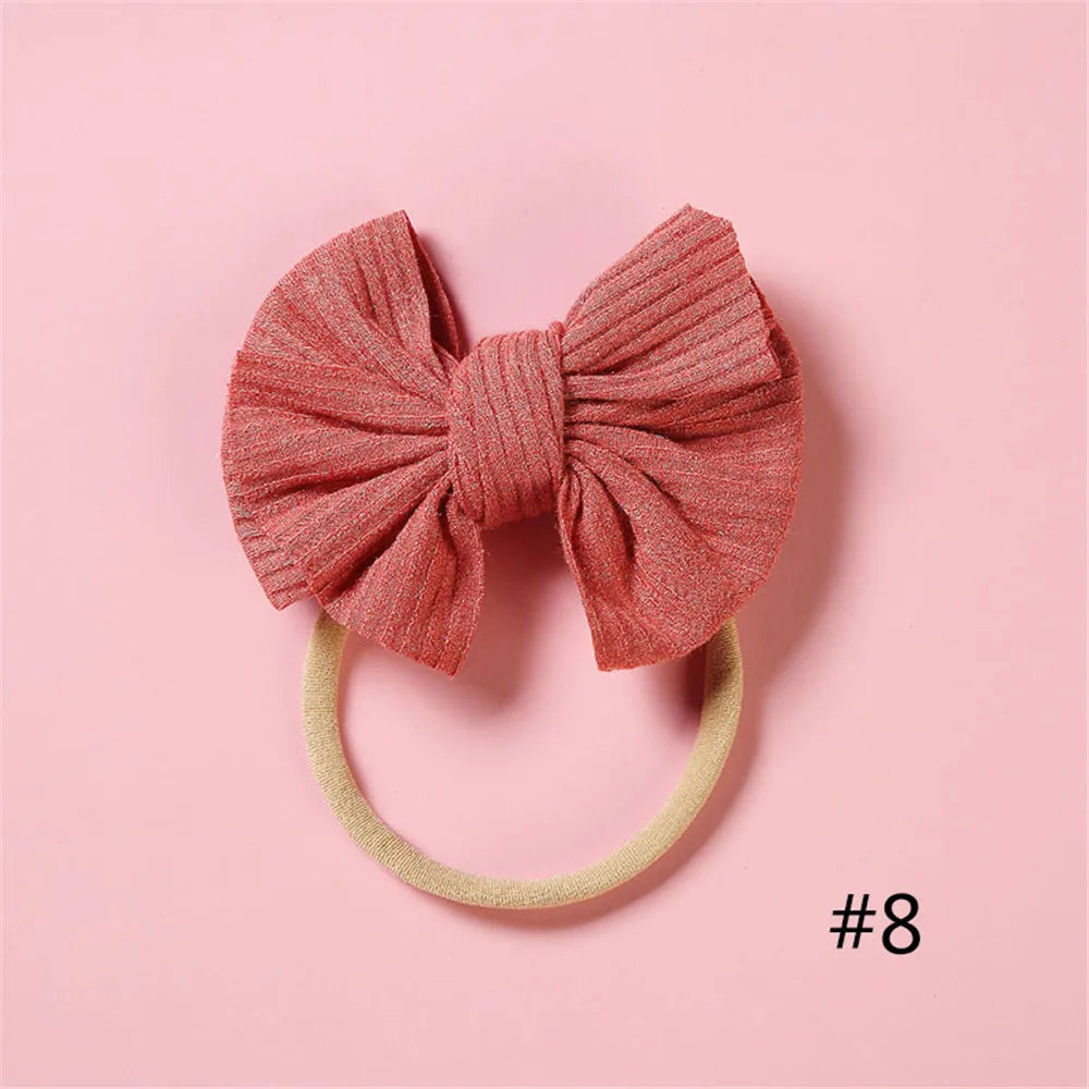 A pink knitted bow headband with a light yellow elastic band on a pink background.