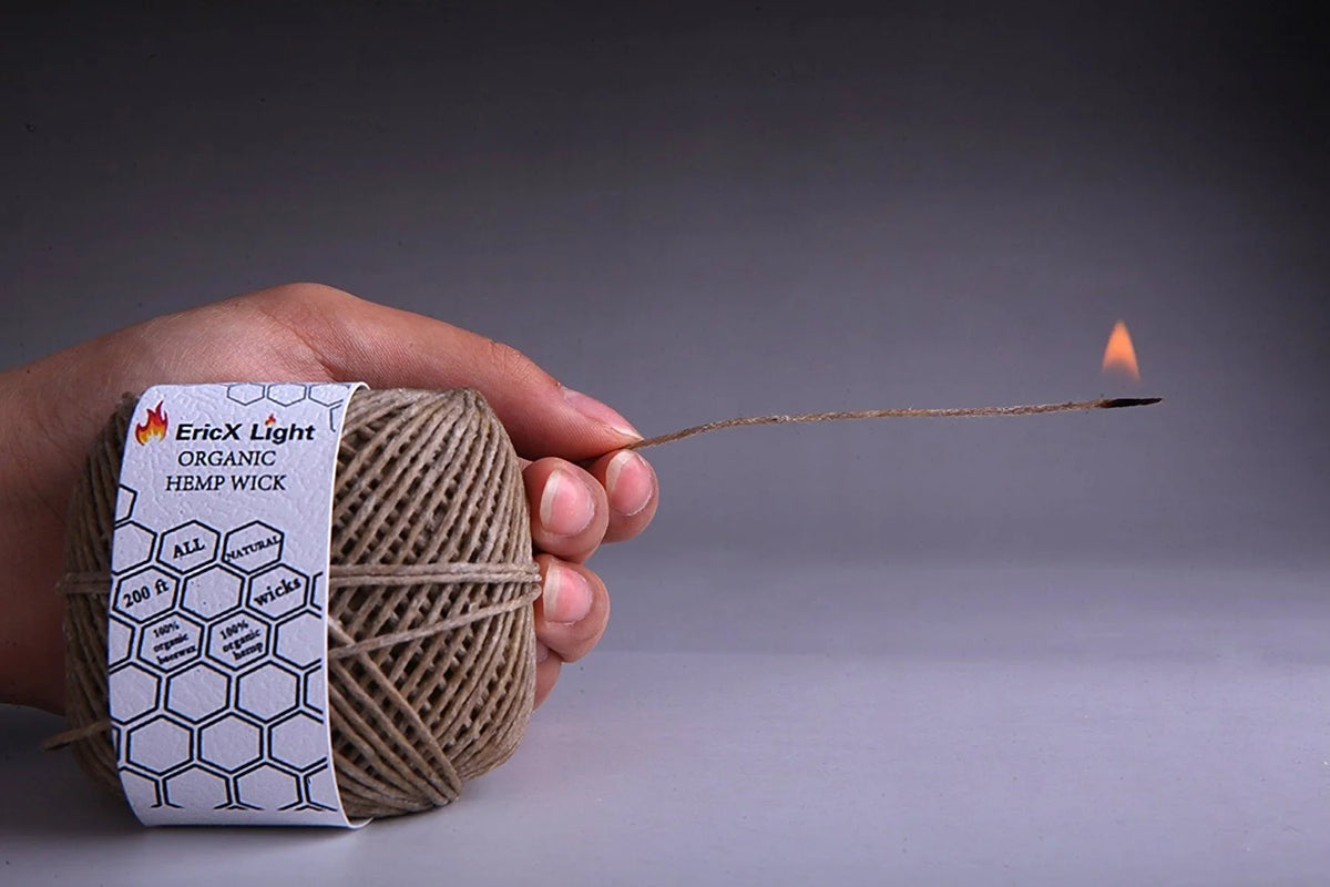 A hand holds a 200-foot organic hemp wick, which is lit and smoking.