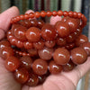 A hand holds a strand of reddish-brown, spherical gemstone beads for jewelry making.