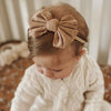 A baby girl wearing a beige bow headband and a white knitted sweater.